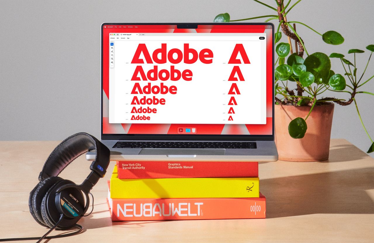 Imagem de um laptop exibindo variações do logotipo Adobe em vermelho.